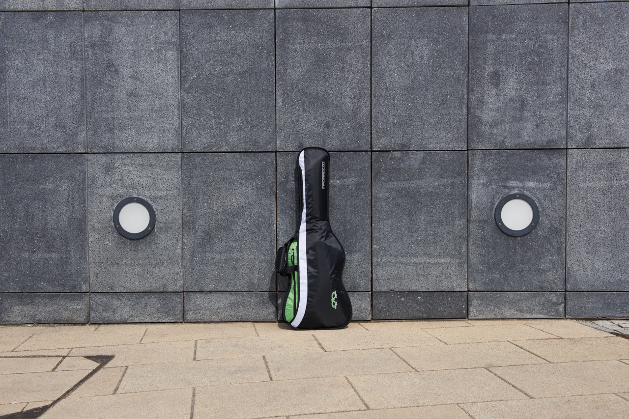 Black MADAROZZO guitar gig bag with green accents standing in front of a modern dark gray tiled building facade.